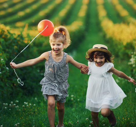 Two little girls with red balloon running together on the field at summer daytime